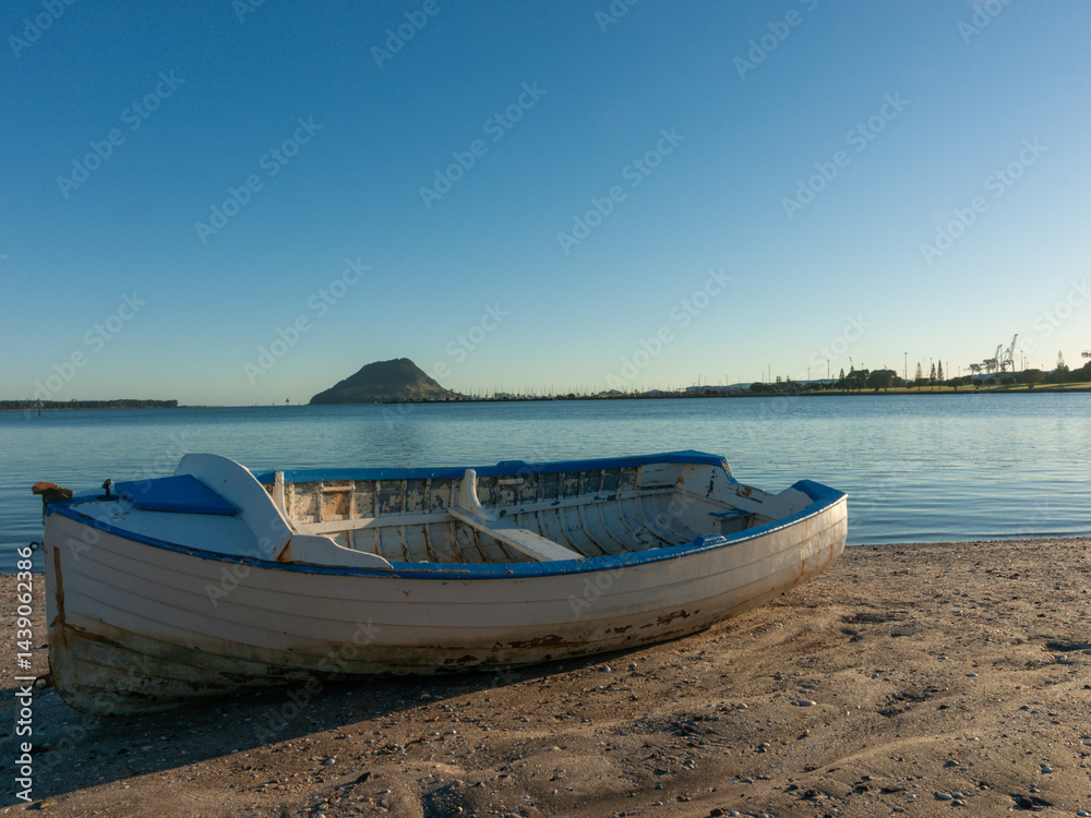 Old blue and white wooden clinker dinghy on beach at mid-tide with landmark Mount Maunganui in background