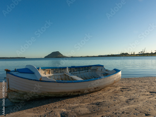Obraz na płótnie Old blue and white wooden clinker dinghy on beach at mid-tide with landmark Mount Maunganui in background w salonie