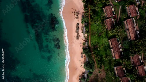 Wallpaper Mural Top-down drone flies along a pristine beach with turquoise water and palm trees, revealing tropical resort villas and rocky shoreline at Silent Beach, Sri Lanka. Torontodigital.ca
