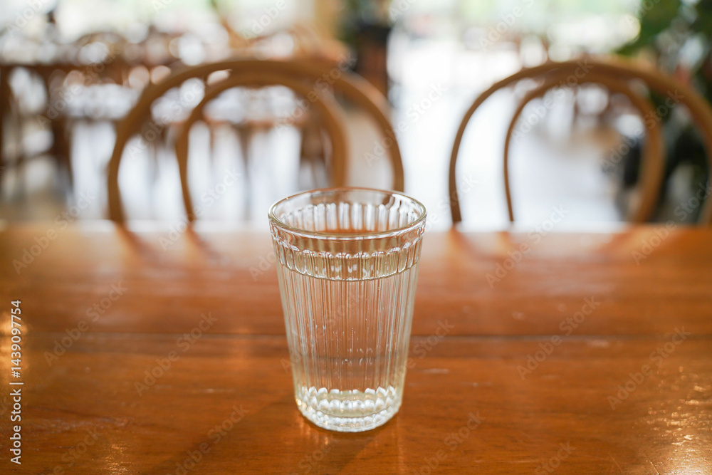 Close-up picture of a glass of water standing on a brown wooden table in a coffee bar