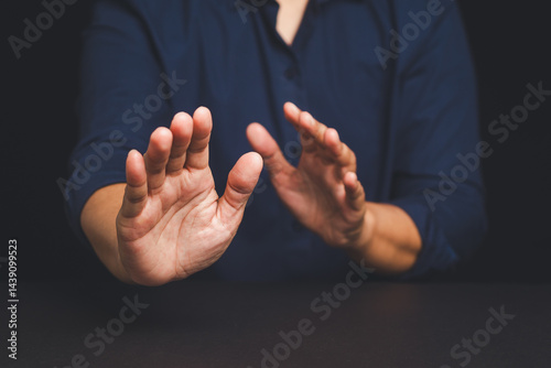 Man in navy shirt raising both hands in defensive stop gesture against dark background.