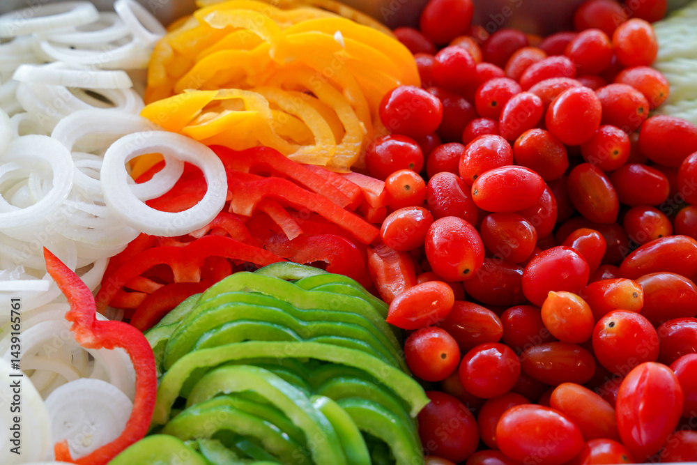Sliced onion, yellow bell pepper, red bell pepper, grape tomato, and green bell pepper arranged in colorful, fresh, healthy salad mix