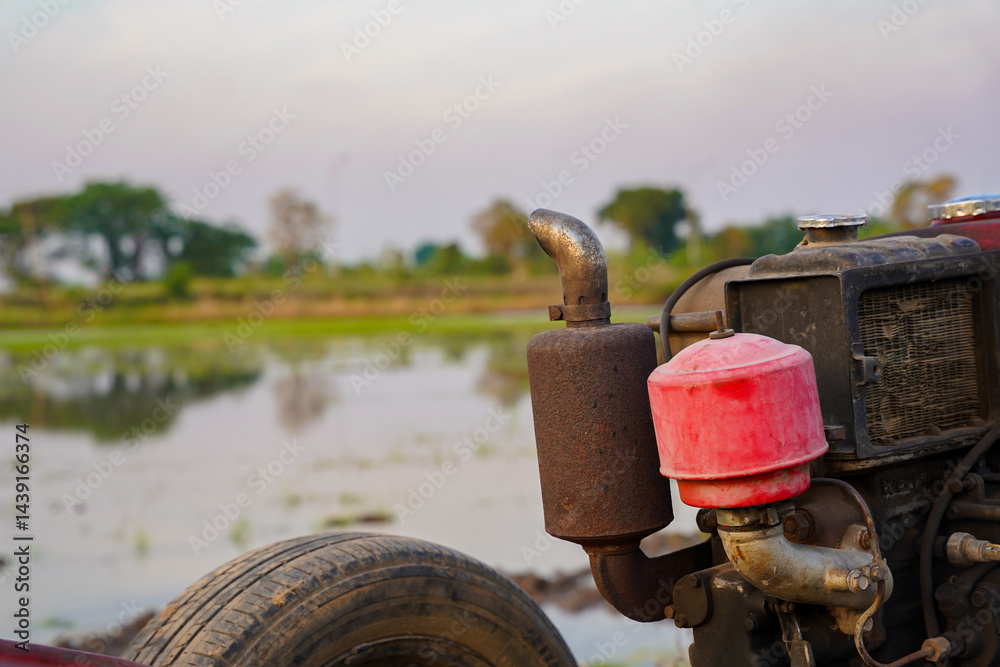 Old tractor engine with red air filter and rusty exhaust pipe near rice field, rural landscape, agriculture machinery, evening light