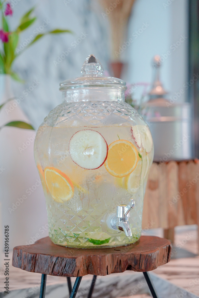 Glass beverage dispenser with lemon and apple slices, refreshing drink on wooden stand, summer party, Infused Water