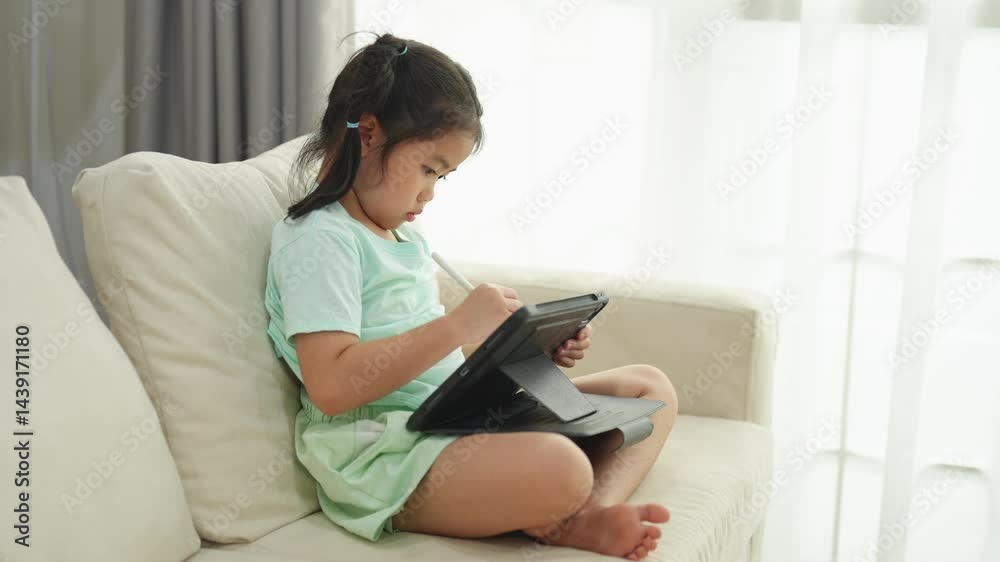 Young Girl Engaged in Digital Learning While Sitting Comfortably on a Couch with a Tablet in a Bright and Cozy Living Room Setting Young Girl Engaged in Digital Learning While Sitting Comfortably on a Couch with a Tablet in a Bright and Cozy Living Room Setting
