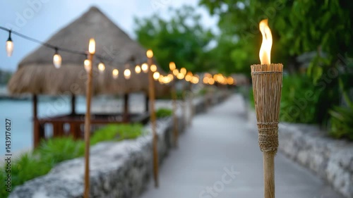 Tiki torch with flame along stone pathway decorated with string light near tropical greenery and thatched hut outdoor evening creating warm inviting