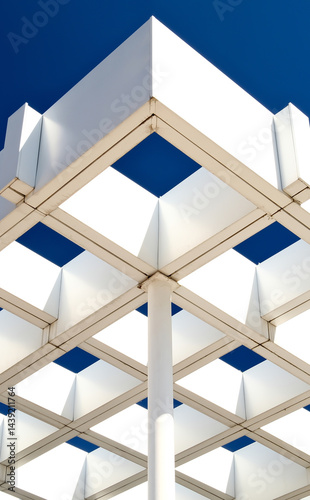 Striking modern architecture with geometric white pergola structure against deep blue sky. Symmetrical grid pattern and minimalist design