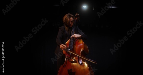 A man plays the double bass in the lamplight. He stands on the stage of the theater