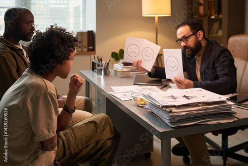 Father and son sitting in front of male psychologist in office and looking at papers with emotions during psychological session