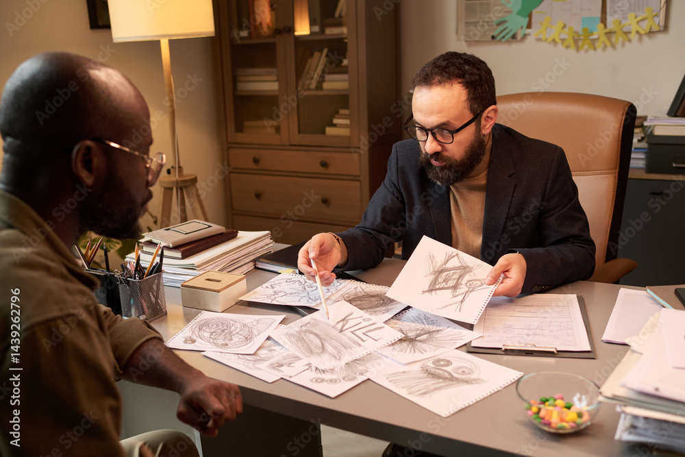 Confident school psychologist pointing at child drawings with aggressive symbols while communicating with parent of schoolchild