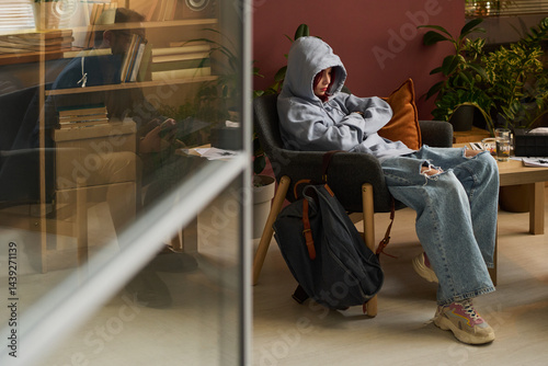Obraz na płótnie Stressed teenager in blue jeans and hoodie sitting in armchair in front of school psychologist during session in office w salonie
