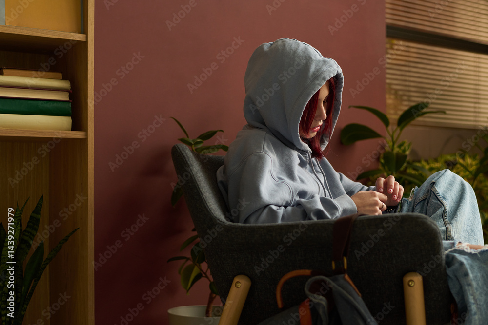 Sad teenage girl in blue casual attire sitting in arm chair in psychologist office and sharing her problem during session