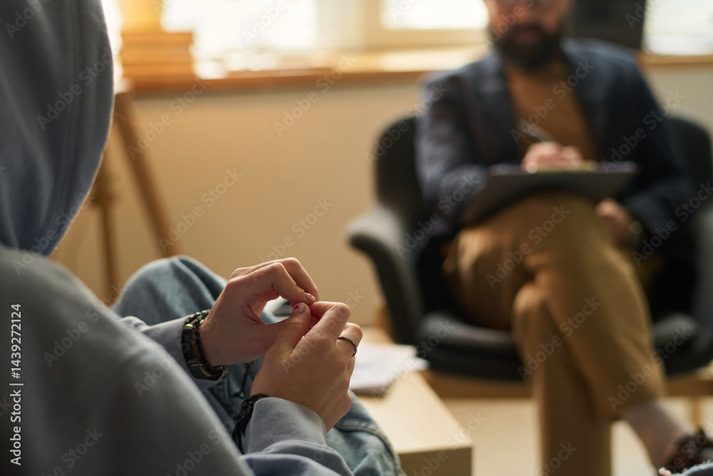 Hands of teenage girl wearing blue hoodie sitting in front of school psychologist during discussion of her problem