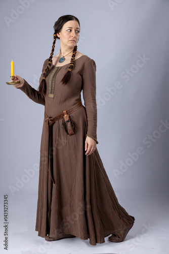 A Medieval peasant woman wearing a rough linen dress called a kirtle with a leather belt and pouch. She has long, dark hair arranged into long plaits photo