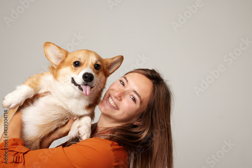 Smiling woman with adorable Corgi dog in studio, joyful pet love moment.
