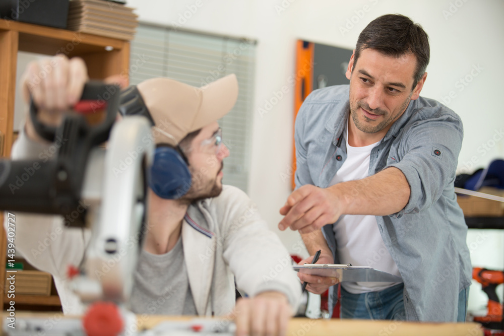 Obraz premium portrait of senior carpenter teaching apprentice standing in workshop