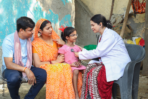 Indian female doctor check heart beat of little girl child sitting with her parents. Rural parents with her daughter getting regular health checkup. Social service. Government of india scheme.
