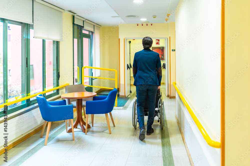 Nurse pushing elderly patient in wheelchair along nursing home corridor
