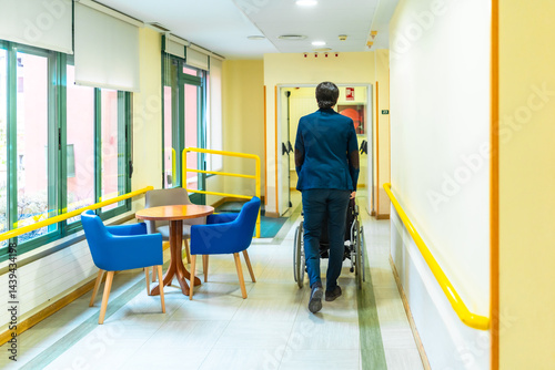 Nurse pushing elderly patient in wheelchair along nursing home corridor