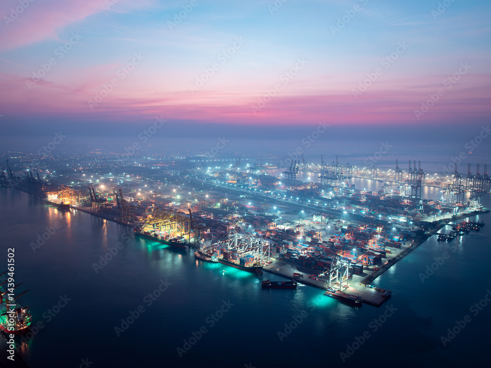 Obraz premium night scene of commercial port load unloading cargo from container ship import export by crane for distributing goods by trailers transported to customers and dealers,