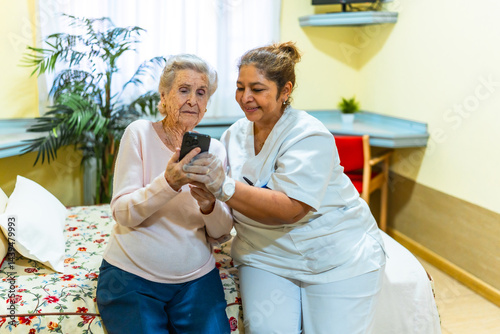 Obraz na płótnie Nurse assisting elderly woman with smartphone in nursing home w salonie