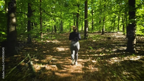 Girl jogging through a sunlit forest trail, surrounded by lush green trees and soft light filtering through the canopy.