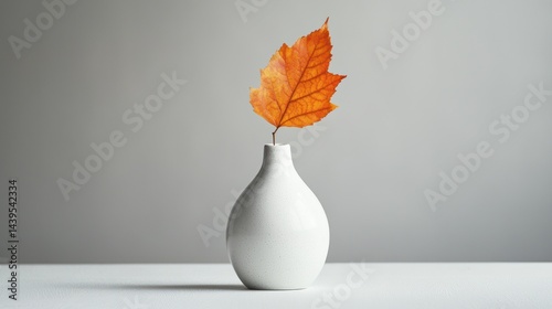 A single leaf in a white ceramic vase against a plain background