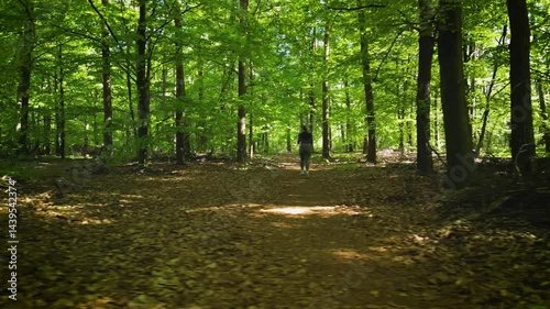 Girl jogging through a sunlit forest trail, surrounded by lush green trees and soft light filtering through the canopy.