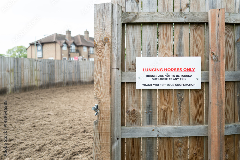 Shallow focus of a racehorse lunging sign seen at the entrance to a racehorse lunging area. Note the circular fencing.
