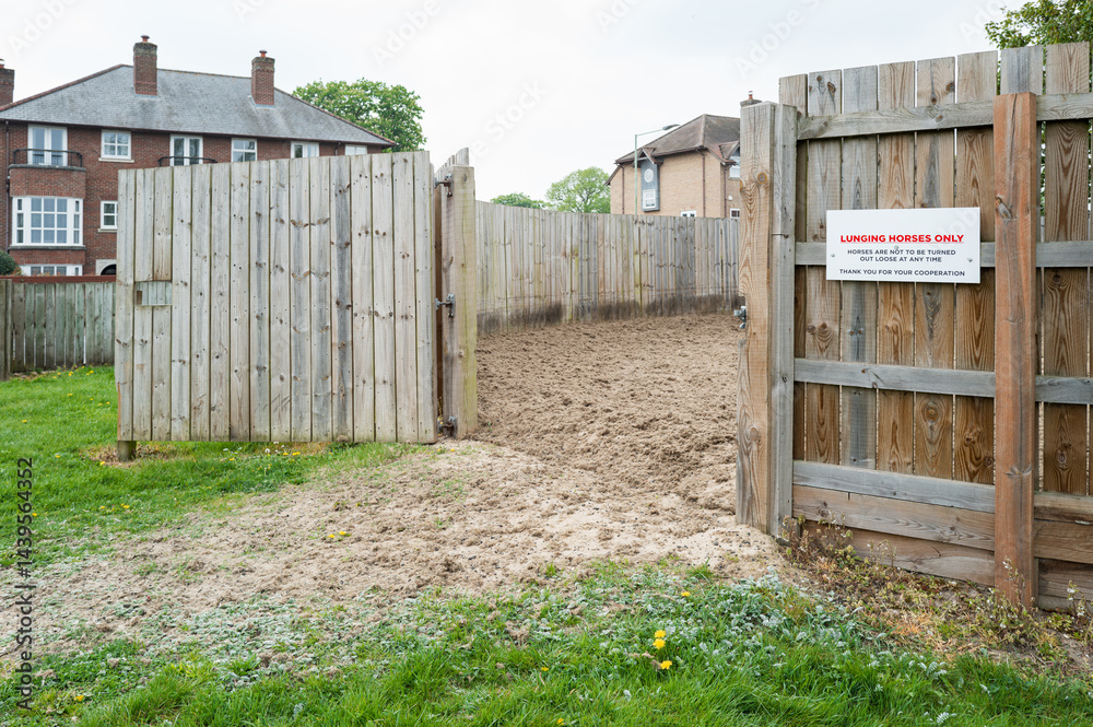 Shallow focus of a racehorse lunging sign seen at the entrance to a racehorse lunging area. The wooden gate is open to allow a racehorse in to be lunged.