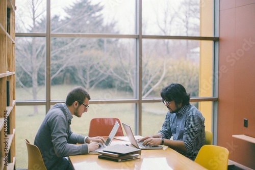 Two young business people, colleagues use laptops in modern office. Happy team working together, discussing solutions