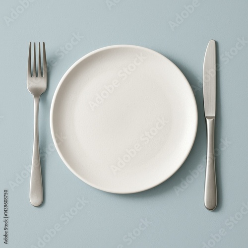 A top-down view of a minimalistic, modern dining setup featuring a sleek, white plate with subtle texture on a soft, pastel blue background.