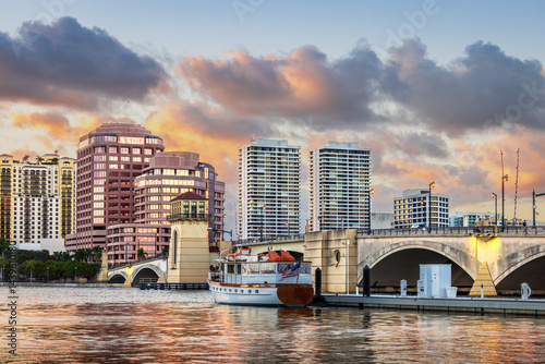 Sunset view of West Palm Beach, Florida, showing a colorful sky, modern city skyline, yachts at the marina, historic bridge, and calm water reflections. Perfect for travel, cityscape, and architecture