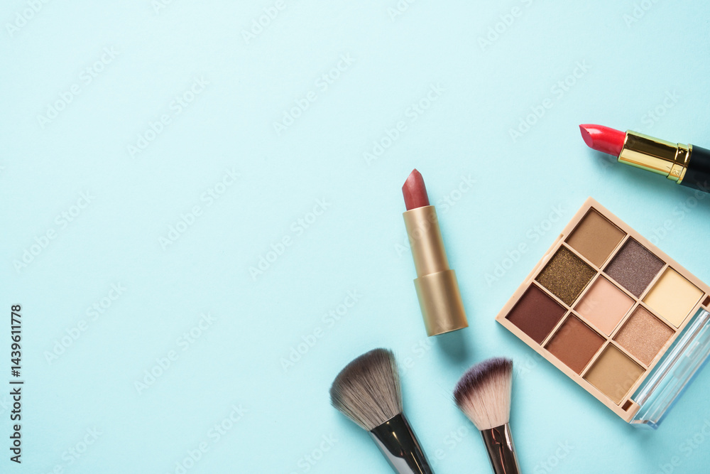 Beauty products on blue background. Cosmetic palette, brushes and lipsticks. Top view.