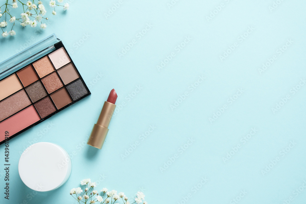 Cosmetic palette, cream, lipstick and white flowers on blue.