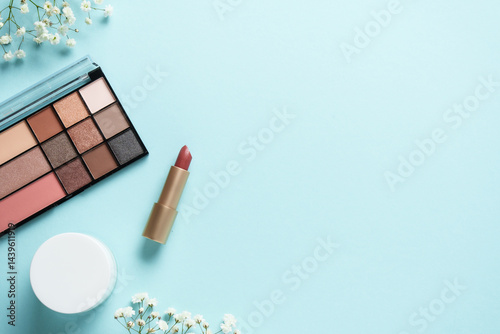 Obraz na płótnie Cosmetic palette, cream, lipstick and white flowers on blue. w salonie