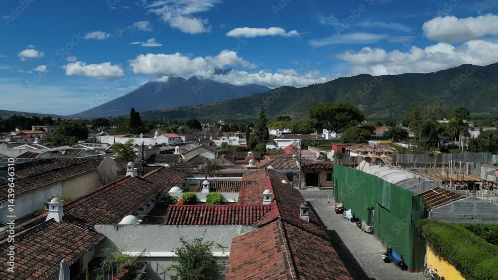 aerial view of antigua guatemala with red shingle rooftops and volcanoes agua fuego and acatenango peaks in the clouds on bright sunny day (volcano mountain travel tourism hiking destination) latin