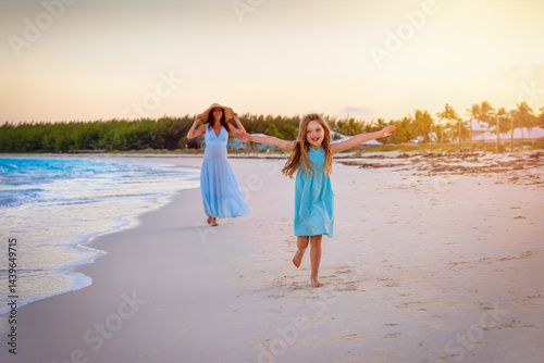 Obraz na płótnie Travel concept with a happy holiday girl and her mother running on a beautiful, tropical beach during sunset time w salonie