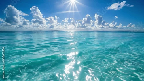 A beautiful blue ocean with a sun shining on the water. The sun is reflected in the water, creating a sparkling effect. The sky is mostly clear, with only a few clouds scattered throughout