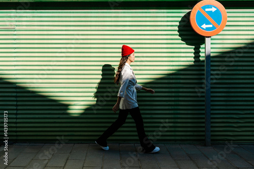 Young woman walking by corrugated wall on sunny day