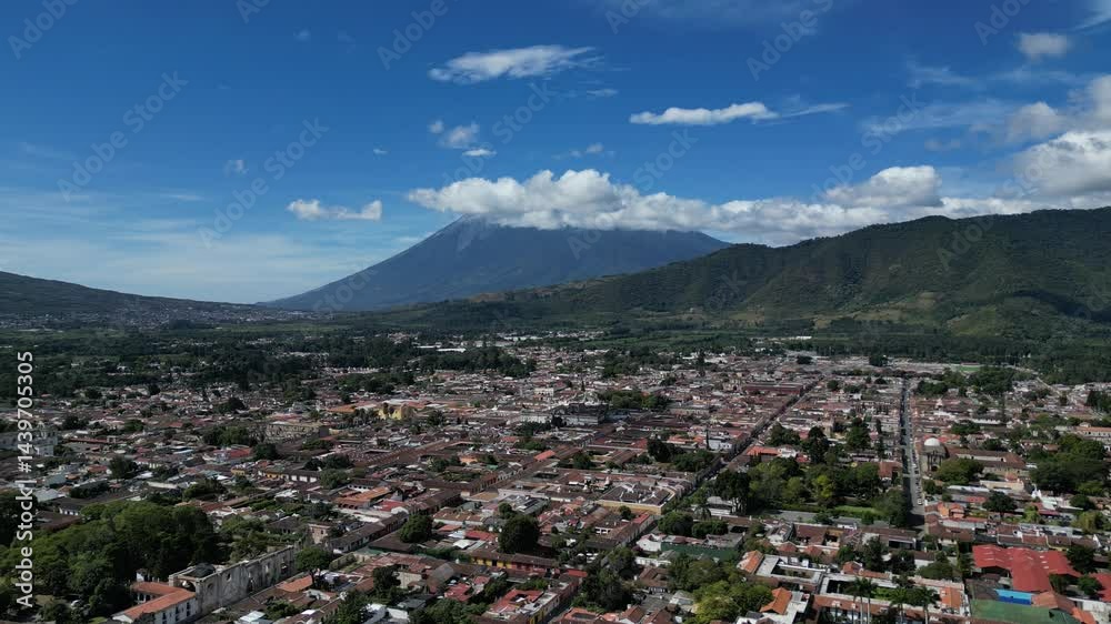 aerial view of antigua guatemala with red shingle rooftops and volcanoes agua fuego and acatenango peaks in the clouds on bright sunny day (volcano mountain travel tourism hiking destination) latin