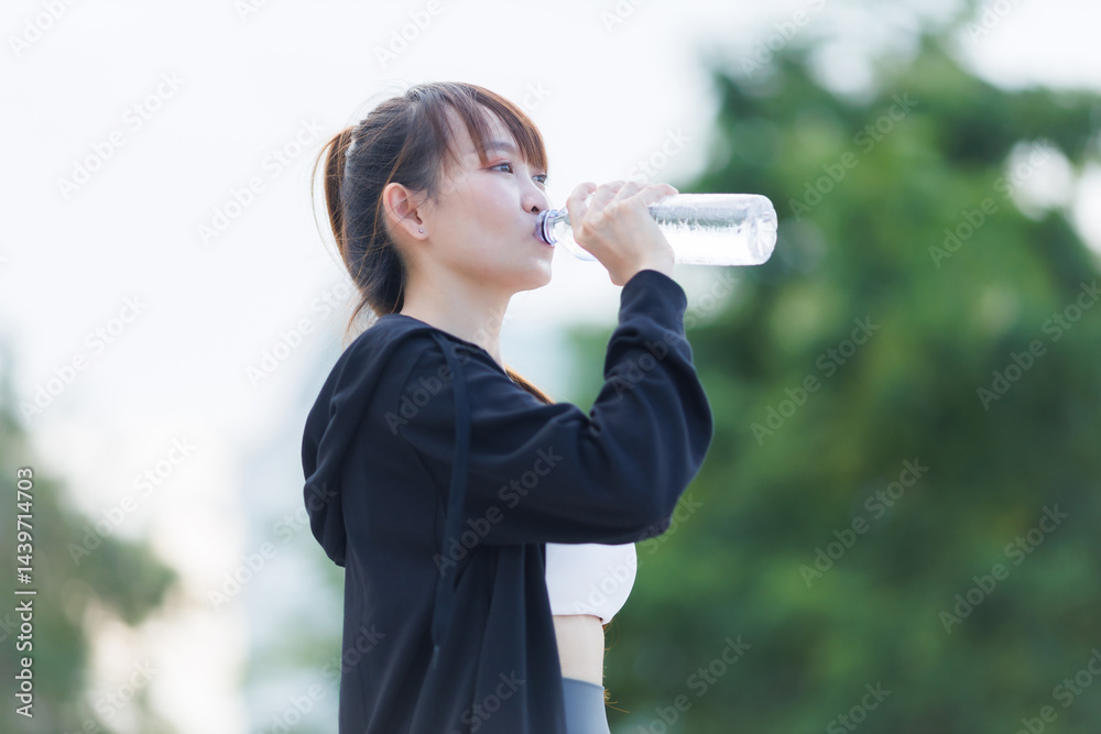 Portrait of beautiful asian Young woman in Black robe sportswear and drinks water working out outside. training on public equipment in outdoor at park. concept Exercise Healthy lifestyle.