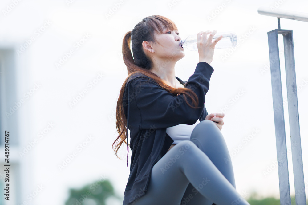 Portrait of beautiful asian Young woman in Black robe sportswear and drinks water working out outside. training on public equipment in outdoor at park. concept Exercise Healthy lifestyle.