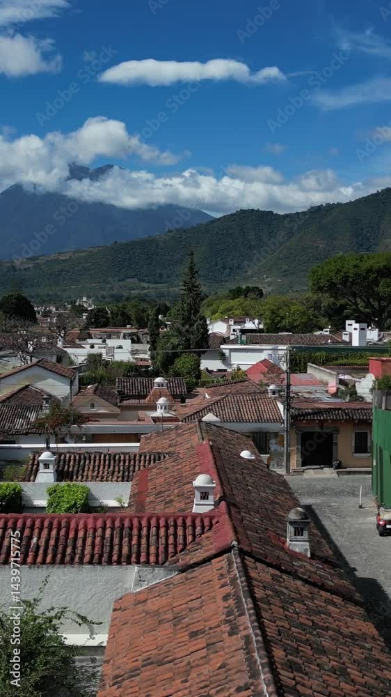 aerial view of antigua guatemala with red shingle rooftops and volcanoes agua fuego and acatenango peaks in the clouds on bright sunny day (volcano mountain travel tourism hiking destination) latin