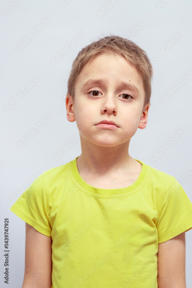 Naklejka premium Young child with short hair wearing a light green t-shirt looks slightly sad. The child stands facing the camera with visible facial features conveying a thoughtful expression