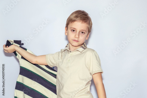 Wallpaper Mural Young boy with short blond hair in a light polo shirt holds a striped shirt in his left hand, gazing confidently at the camera. His expression is calm and composed Torontodigital.ca