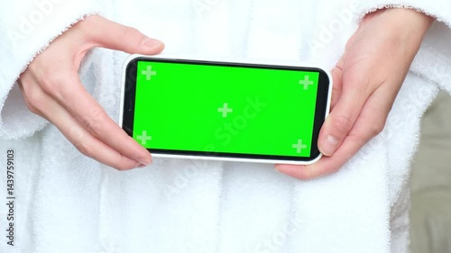 Close-up of hands with a white phone. Green screen, finger. The movement of women's fingers on the monitor. A girl in a bathrobe in a hotel, watching a video, an advertisement. High quality 4k footage