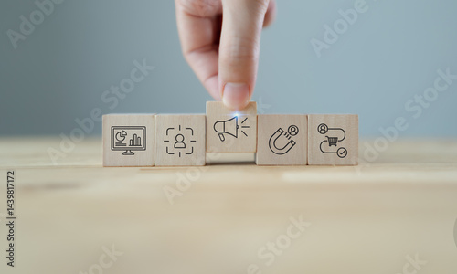 Marketing strategy planning with wooden blocks. A hand arranging wooden blocks with  icons representing data analytics, customer targeting, advertising, lead generation and sales process.