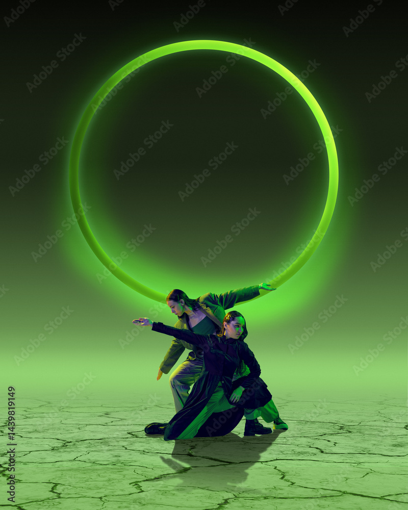 Two female dancers in futuristic pose with green glowing ring dramatically dancing on cracked desert floor. Contemporary art. Concept of dance, futurism, art, youth culture. Poster design