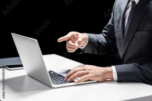 Businessman using laptop while touching or pointing at the laptop screen. Cellphone and tablet on the table. Mockup and copy space. Business and technology concept